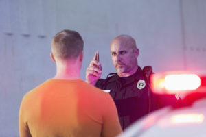 Police officer giving sobriety test to young man to see if he is driving under the influence of drugs or alcohol. Police cruiser is out of focus in the foreground.